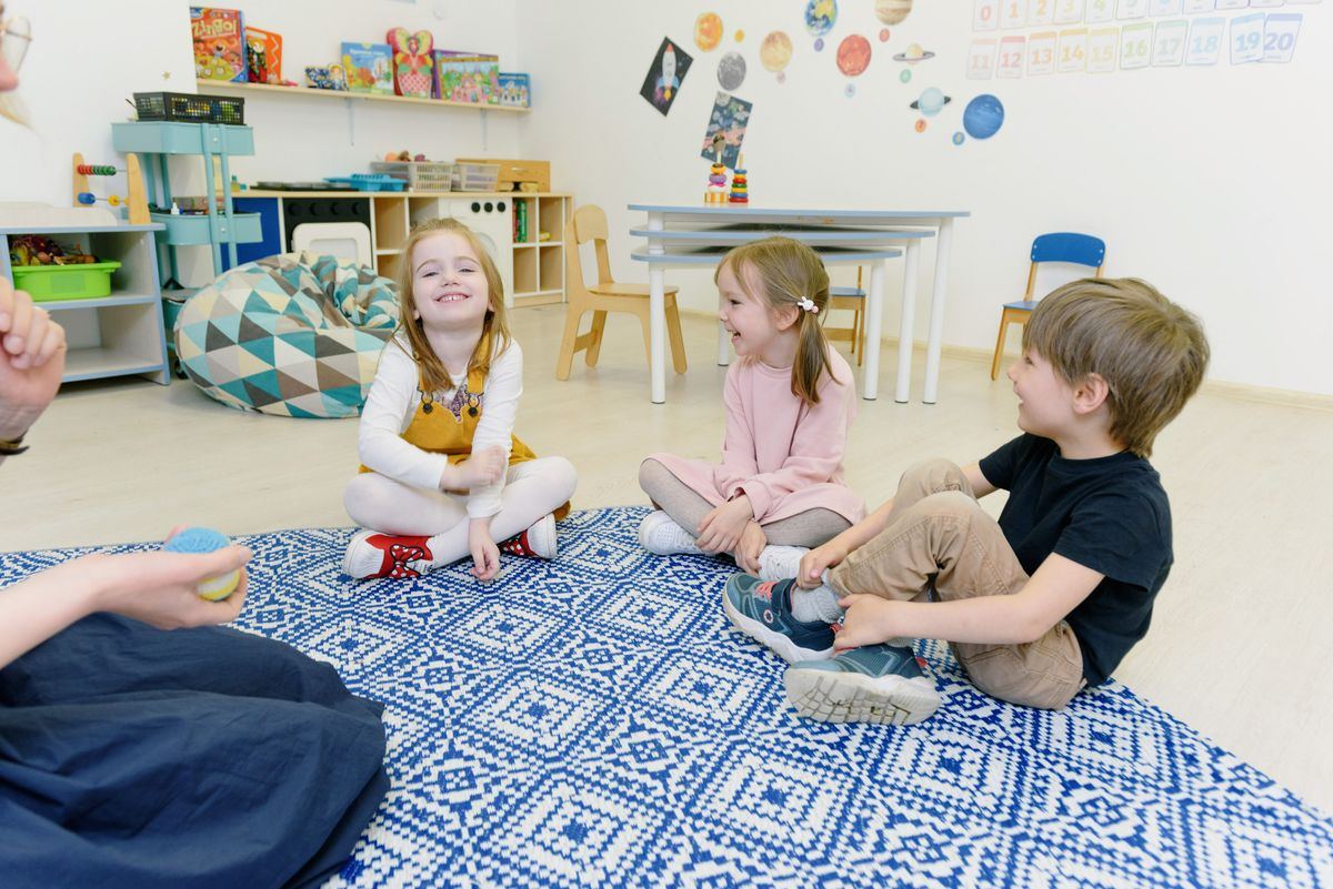 Children sitting in circle time with their educator on a classroom rug